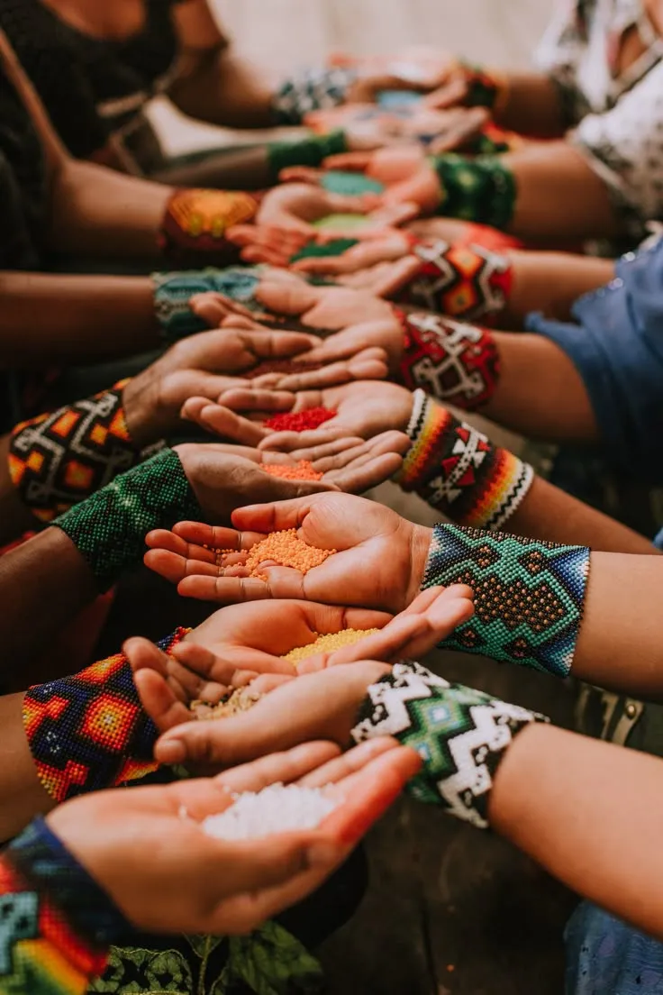 Many hands in a row holding loose beads and wearing beaded cuffs — the project’s community.